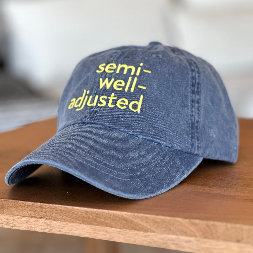 Blue cap with 'semi-well-adjusted' text on a wooden surface