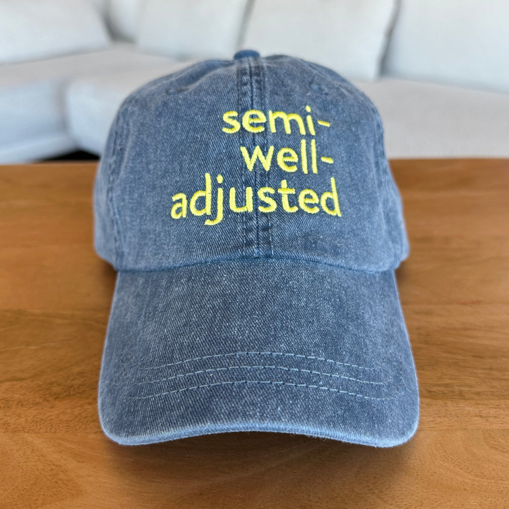 Blue cap with 'semi-well-adjusted' text on a wooden surface