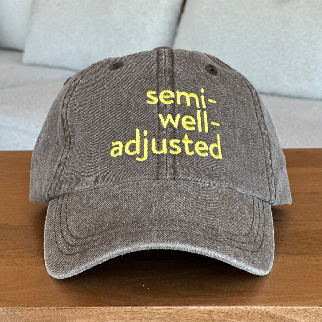 Brown cap with 'semi-well-adjusted' text in yellow on a wooden surface.