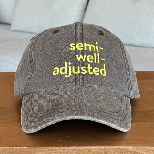 Brown cap with 'semi-well-adjusted' text in yellow on a wooden surface.